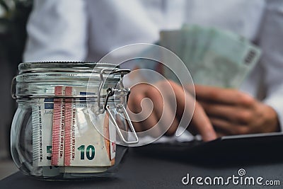 Man hands counting expenses banknotes of euro cash from glass jar in the piggy bank on calculator. Close up of hands Stock Photo