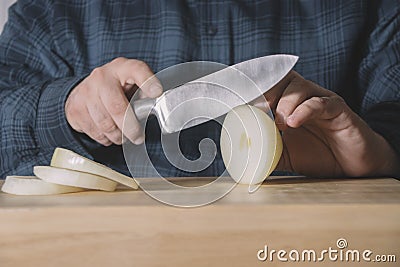 Man hands cutting with a sharp knife an onion in slices on a wooden table. Burger concept Stock Photo