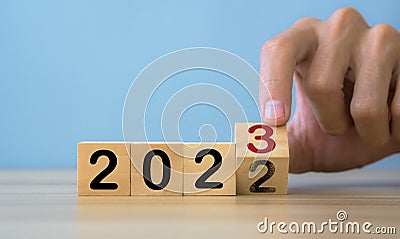 Man hands flipping of 2022 to 2023 on wooden block cube.happy new year 2023.Teble and blue background Stock Photo