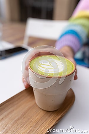 Man Hands Holding Macha Latte Cup with Wooden Plate in Caffe Stock Photo