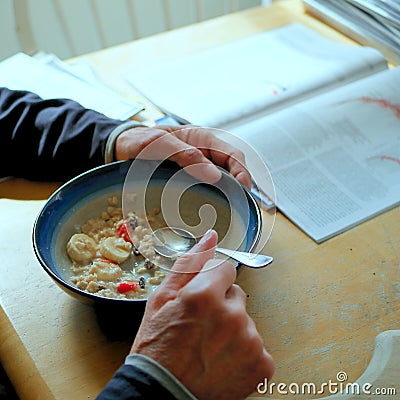 Man with hands in the morning, eating breakfast oatmeal with strawberries and bananas at his kitchen table. Stock Photo