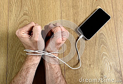 Man hands wrapped on wrists with mobile phone cable handcuffed in smart phone networking addiction concept Stock Photo