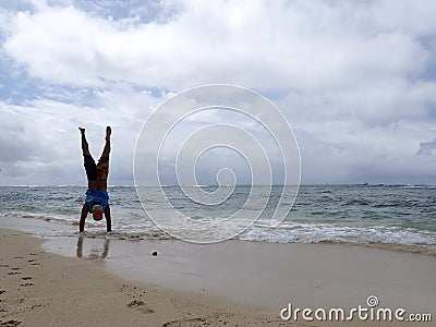 Man Handstand on beach as wave roll into Shore Stock Photo