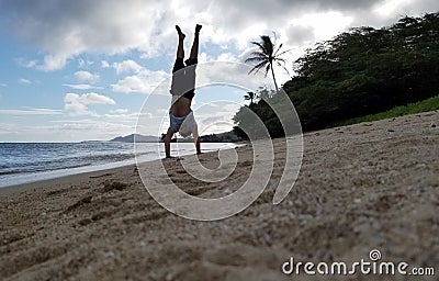 Man Handstand on beach as wave roll on to shore Stock Photo