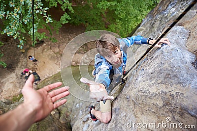 Climber rock climbing overhanging cliff with rope. Asking for help. Man helping his friend to climb a rock. Stock Photo
