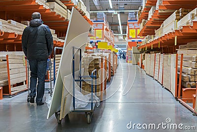 A man in a hardware store. Carts loaded with boards. shop of building materials. Racks with boards, wood and building material. Stock Photo