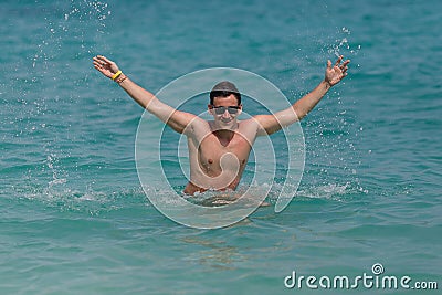 Man has fun in the blue sea by jumping up and spashing water. Stock Photo