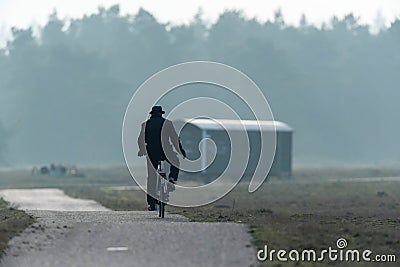 Man in hat cycling on path in misty nature reserve. Stock Photo