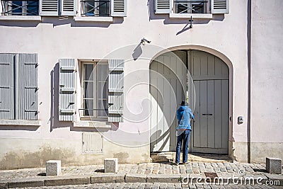 Man in hat peers into the courtyard of the house with shutters through slightly open gate Stock Photo