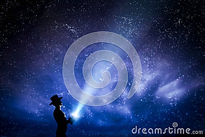 Man in hat throwing light beam up the night sky full of stars. To explore, dream, magic. Stock Photo