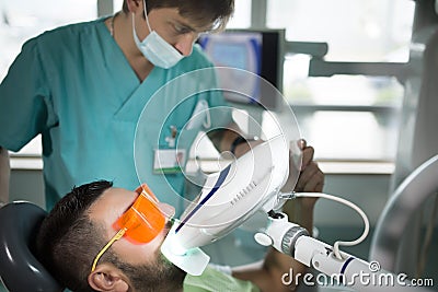 Man having teeth whitening by dental UV whitening device,dental assistant taking care of patient.Eyes protected with glasses Stock Photo