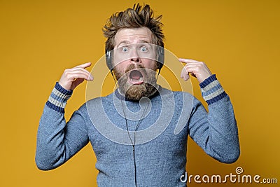 Man in the headphones is ecstatic and shocked. Shaggy music fan in an sweater stares in amazement at the camera with Stock Photo