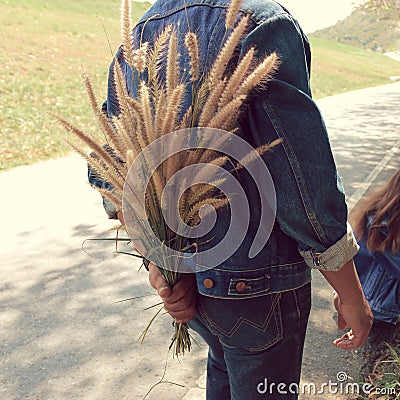 The man hides the grass flowers behind his back to surprise his girlfriend Stock Photo