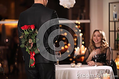 Man hiding roses for his beloved woman in restaurant at Valentine`s day dinner Stock Photo