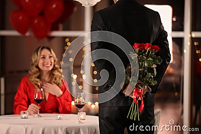 Man hiding roses for his beloved woman in restaurant at Valentine`s day dinner Stock Photo