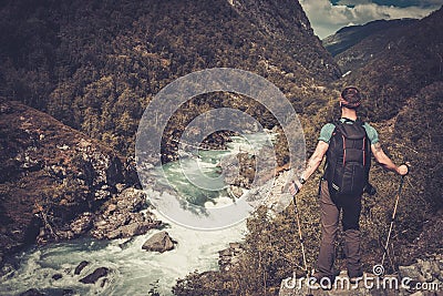 Man hiker with backpack standing on the edge of the cliff with epic wild mountain river view. Stock Photo