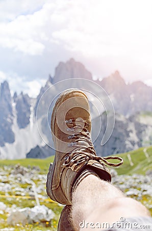 Man hiker lie on a ground. Peaks like a background. Sunny day.Trekking boots.Lens flare. Succesful backpacker enjoy a view. Stock Photo