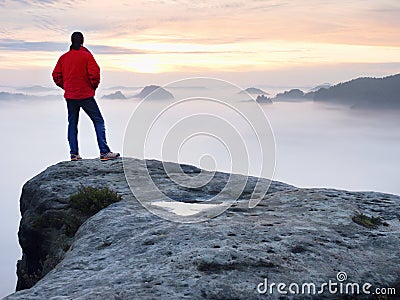 Man hiker at mountain peak. Marvelous daybreak in autumn misty landscape. Sun hidden in clouds Stock Photo