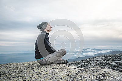 Man hiker sitting in a yoga pose at the peak of the mountain in the summer. Meditation after a long climb on a mountain Stock Photo