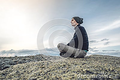 Man hiker sitting in a yoga pose at the peak of the mountain in the summer. Meditation after a long climb on a mountain Stock Photo