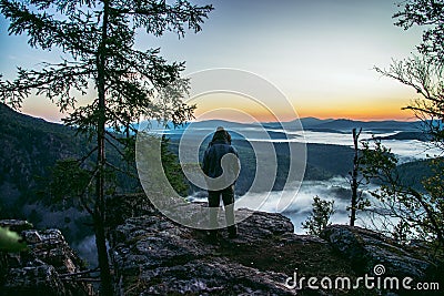 Man hiker standing back on peak of mountains and enjoy to see beautiful landscape view of rocks and mist coming up at Stock Photo