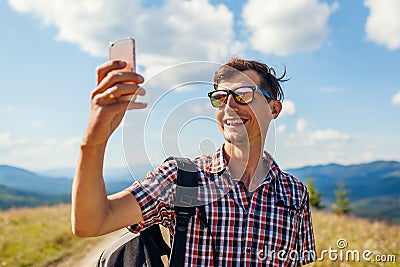 Man hiker taking selfie with smartphone in Carpathian mountains on hill peak. Traveler backpaker enjoys view Stock Photo