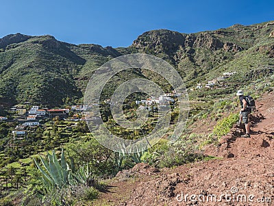 Man hiker watching at scenic landscape with Imada village at hiking trail Barranco de Guarimiar Gorge. Green mountain Stock Photo