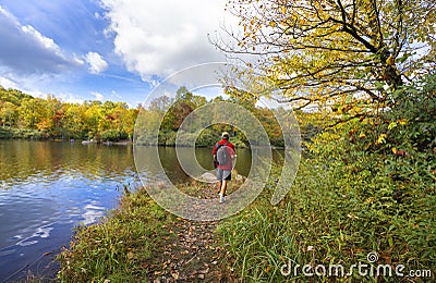 Hiker walking next to the lake in autumn forest. Stock Photo