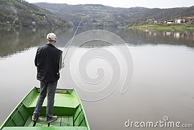Man With His Back Towards Camera Fishing From The Boat Reeling String And Waiting Fish To Take A Bait Water Reflection Stock Photo