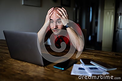 A man with his hands on his head in shock looking at a laptop with passports, a cellphone and covid digital certificates Stock Photo