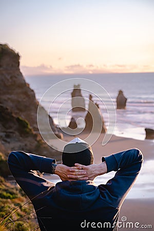 Man with his hands on neck looking at amazing scenic rock formations by the beach Stock Photo