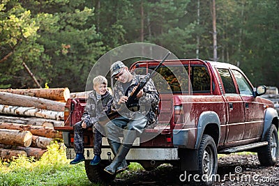 Man at his truck with his son in the forest. Hunter teaches young boy how to use shotgun rifle. Stock Photo
