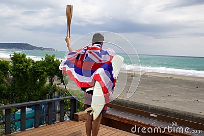 Man hold a torch used in large sporting event , with Hawaiian flag and surfboard. Stock Photo