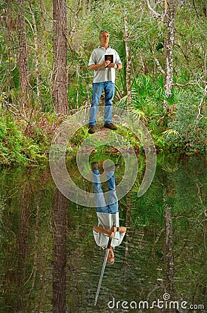 Man holding Bible while his reflection in the water shows him holding a sword representing power of faith Stock Photo