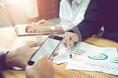 Man holding a blank screen smartphone, on the desk, colleagues are using Laptop and documents. Teamwork ideas work faster. Stock Photo