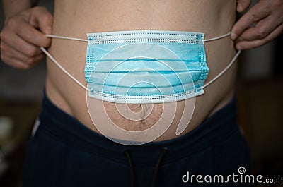A man holding a blue medical mask over his stomach will gain weight during the pandemic of the coronavirus crisis. Stock Photo