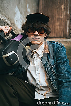 Man holding boombox on his shoulder sitting on stairs. 90s retro style nostalgia concept Stock Photo
