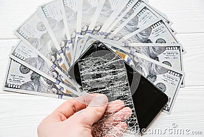 Man is holding broken screen protector tempered glass. Money lying near the phone. Dollar notes Stock Photo