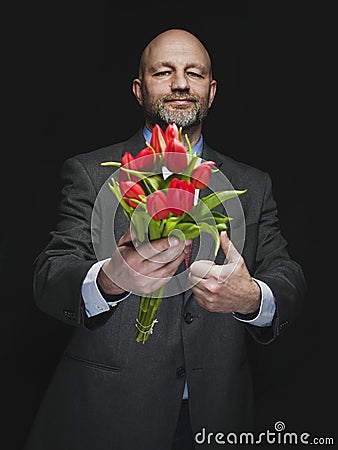 Man holding fresh red tulip bouquet in his hands. Model is bald with grey beard, wearing classic grey suit. Handsome male with Stock Photo