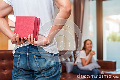 Man holding gift behind him for surprise girlfriend at their home. Woman waiting for Valentines gift form boyfriend. Happy Stock Photo