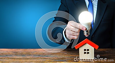 Man is holding a glowing light bulb over the house. Smart home concept. Provision of housing with electricity and communications. Stock Photo