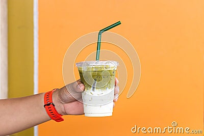 A man holding green tea with milk and iced cup in hand with orange color wall Stock Photo