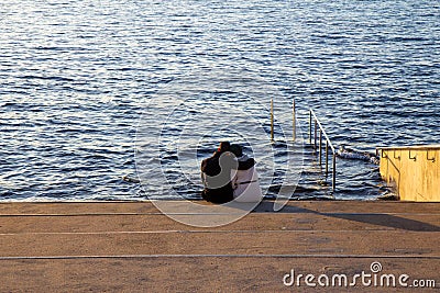 A man is holding his arm around a woman as they sit on a staircase just by the waters edge, looking out to the sea, feeling calm, Stock Photo