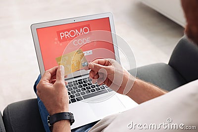 Man holding laptop with activated promo code and credit card on sofa, closeup Stock Photo