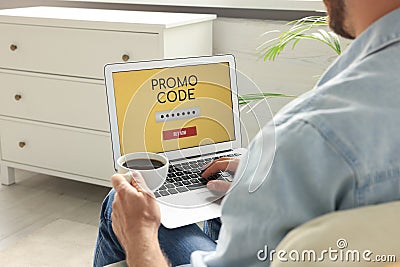 Man holding laptop with activated promo code and cup of coffee indoors, closeup Stock Photo