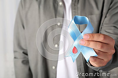 Man holding light blue ribbon with paper blood drop indoors, closeup. World Diabetes Day Stock Photo