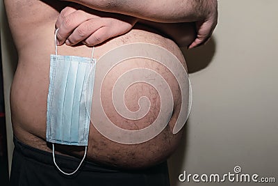 Man holding medical mask gets fat by pandemic of Corona virus crisis. Obesity concept. Stock Photo