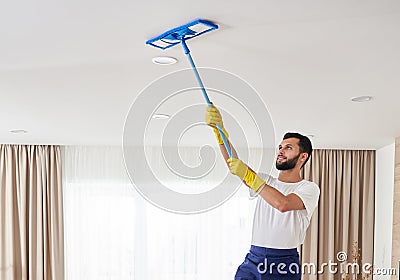 Man cleaning ceiling and lamps in living room. House cleaning service concept. Stock Photo