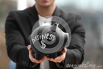 Man holding piggy bank with word BUSINESS against blurred background Stock Photo