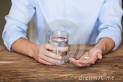 Man holding pills and glass of water at wooden table, closeup Stock Photo